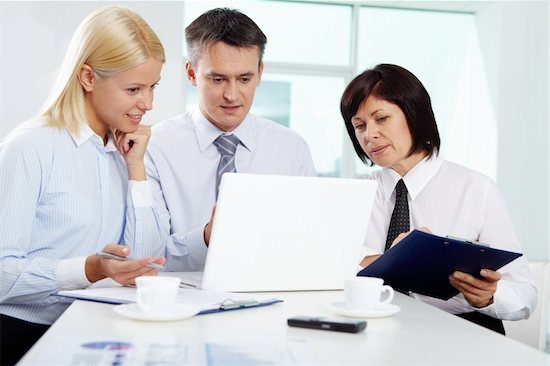 Picture of two businesswomen and one businessman sitting at table looking at laptop screen; pleased expressions hint they're looking at five-star reviews