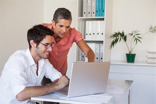 Photo of smiling man sitting at desk and woman peering over his shoulder at laptaop screen. HBS five-star review solicitation services bring smiles to clients' faces.