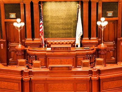 photo of a empty courtroom, all wood desk and partition with two flags on both sides of the judge's seat - one the American flag